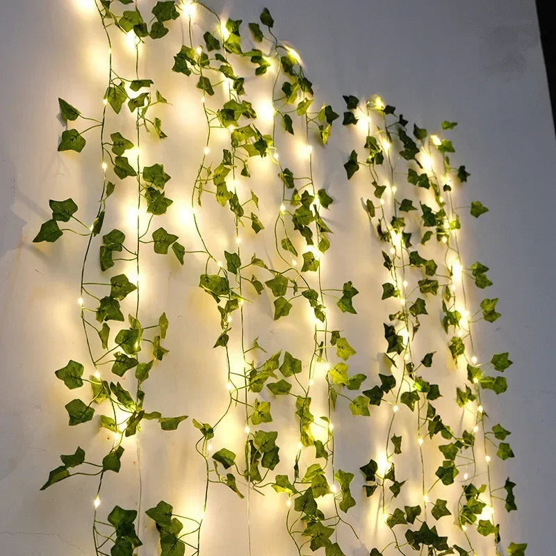 Green artificial ivy vines with warm white fairy string lights hanging on a white wall for decorative indoor ambiance