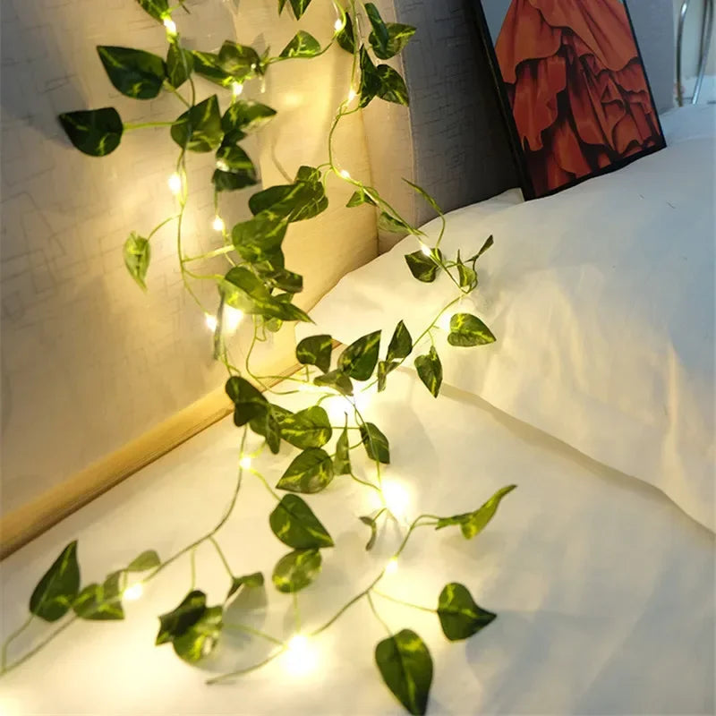 Green ivy vine string lights draped over white bed linens in cozy bedroom setting