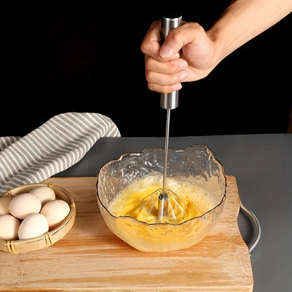 Hand using a stainless steel whisk to beat eggs in a textured glass bowl on a wooden cutting board, next to a basket of eggs