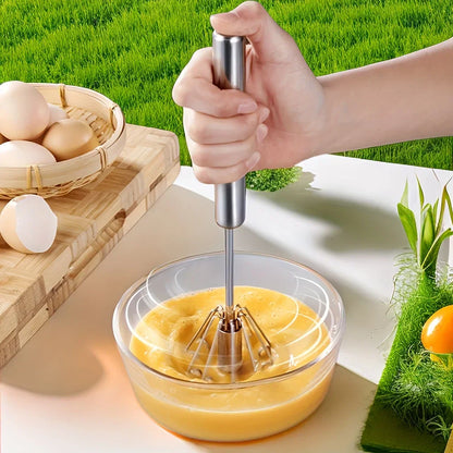 Hand whisking eggs in a glass bowl on a white table with eggs basket and green grass background