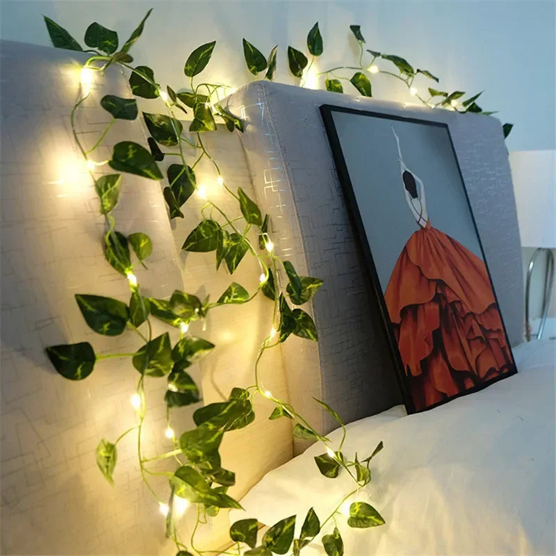 String lights with green leaves draped over a gray headboard with framed painting of a woman in an orange dress