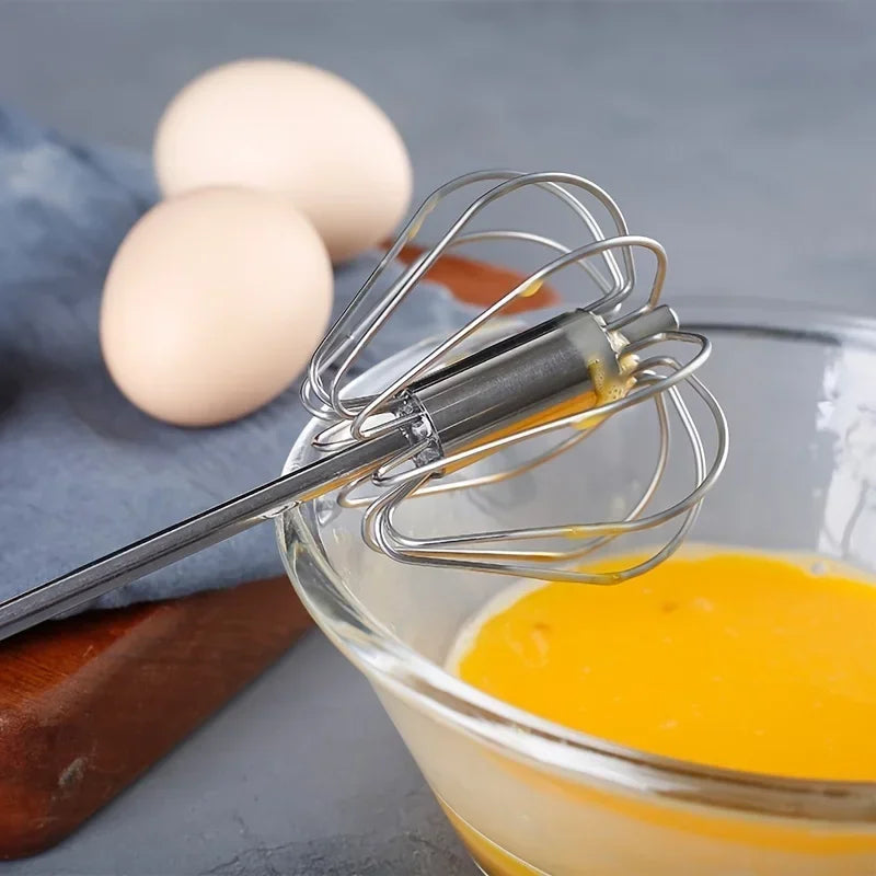 Metal whisk resting on glass bowl with whisked eggs, two whole eggs on cloth background