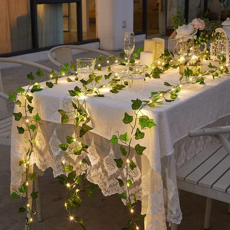 Outdoor dining table with white lace tablecloth decorated with green ivy garland and warm fairy lights