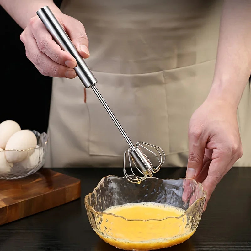 Hand using stainless steel egg beater to whisk eggs in textured glass bowl on kitchen counter
