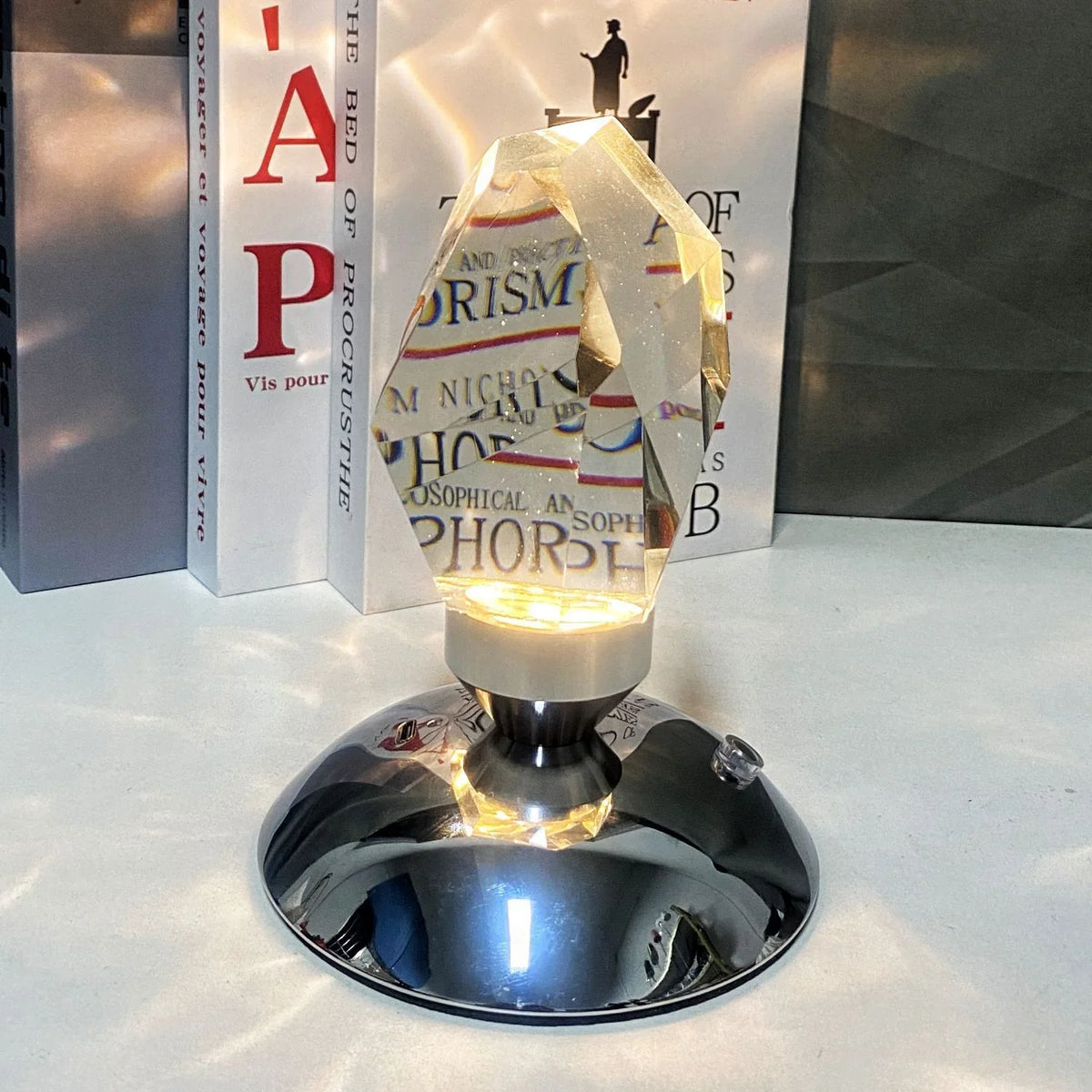 Modern crystal prism lamp with metal base illuminating texts on books in background