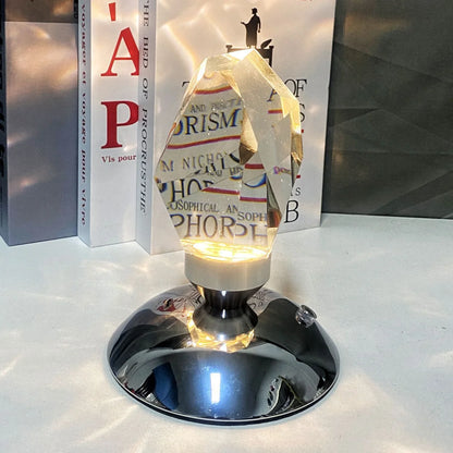 Modern crystal prism lamp with metal base illuminating texts on books in background