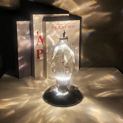 Crystal prism lamp casting light patterns on surface near books including The Black Swan